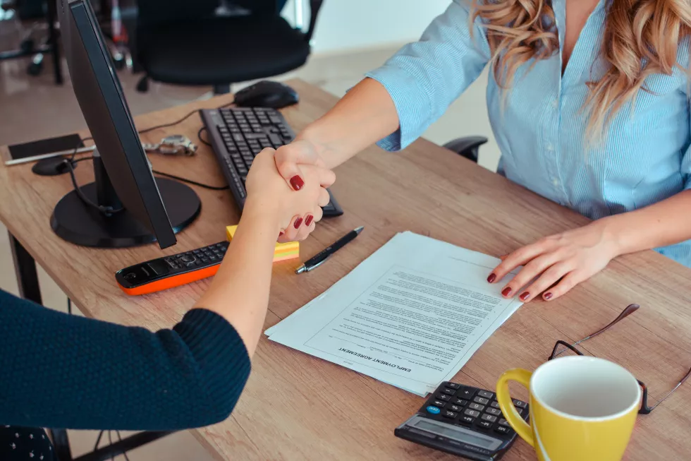 midsection-businesswomen-shaking-hands-desk-office
