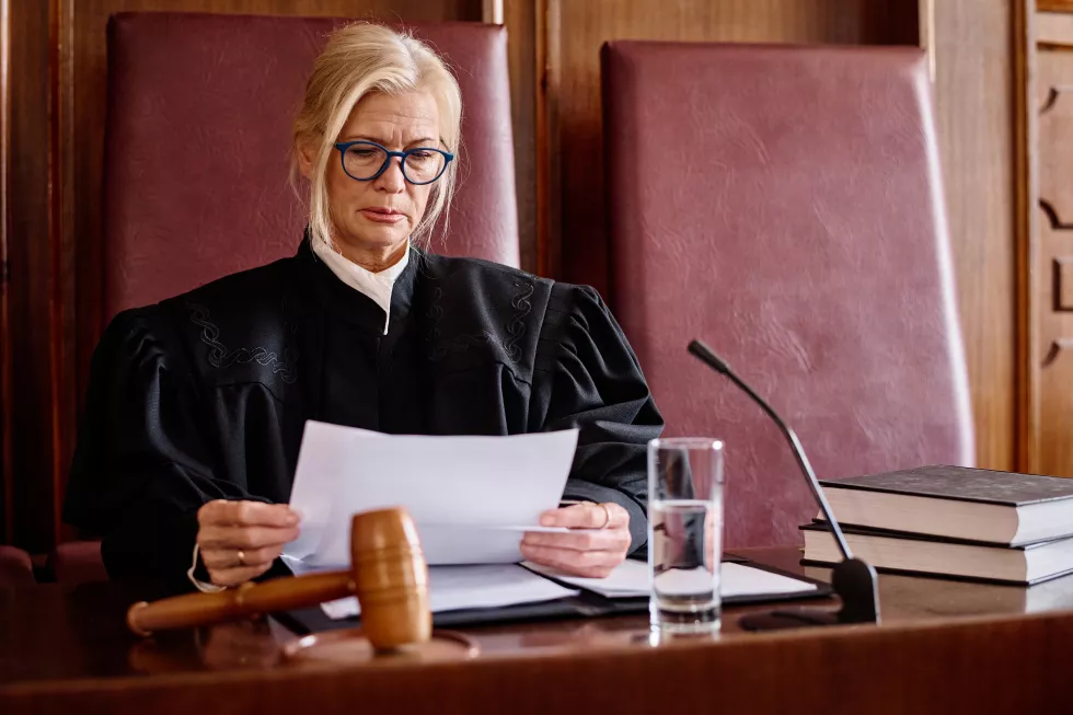 serious-blond-female-judge-black-mantle-looking-through-paper-document-before-trial-session