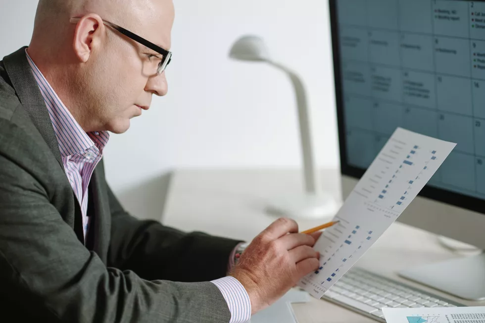 concentrated-mature-businessman-eyeglasses-sitting-desk-with-computer-viewing-statistics-paper