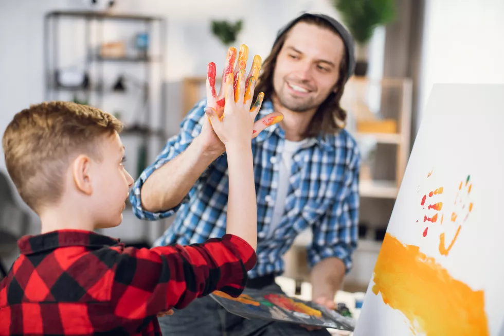 man-giving-high-five-son-while-painting-easel