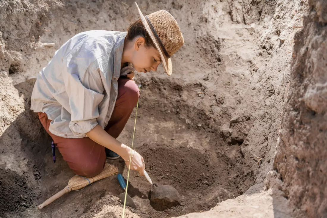 Archeolozka odslania zabytek w wykopie podczas badan terenowych
