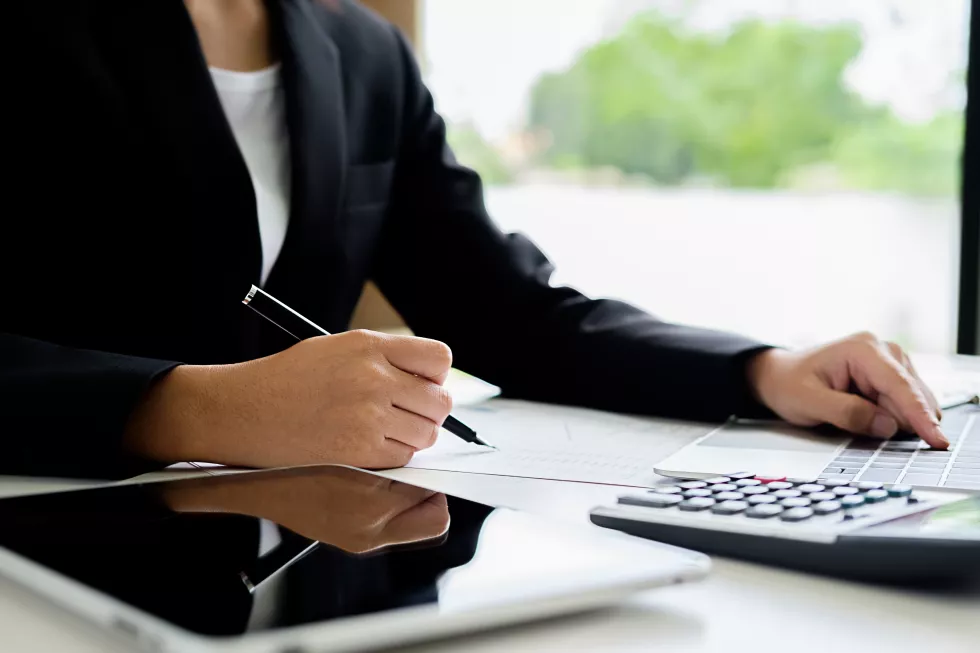 midsection-woman-writing-paper-while-using-laptop-desk