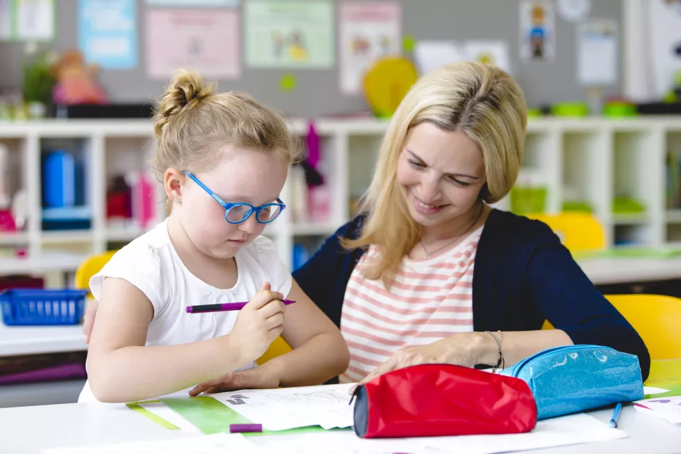 smiling-teacher-teaching-girl-table-school