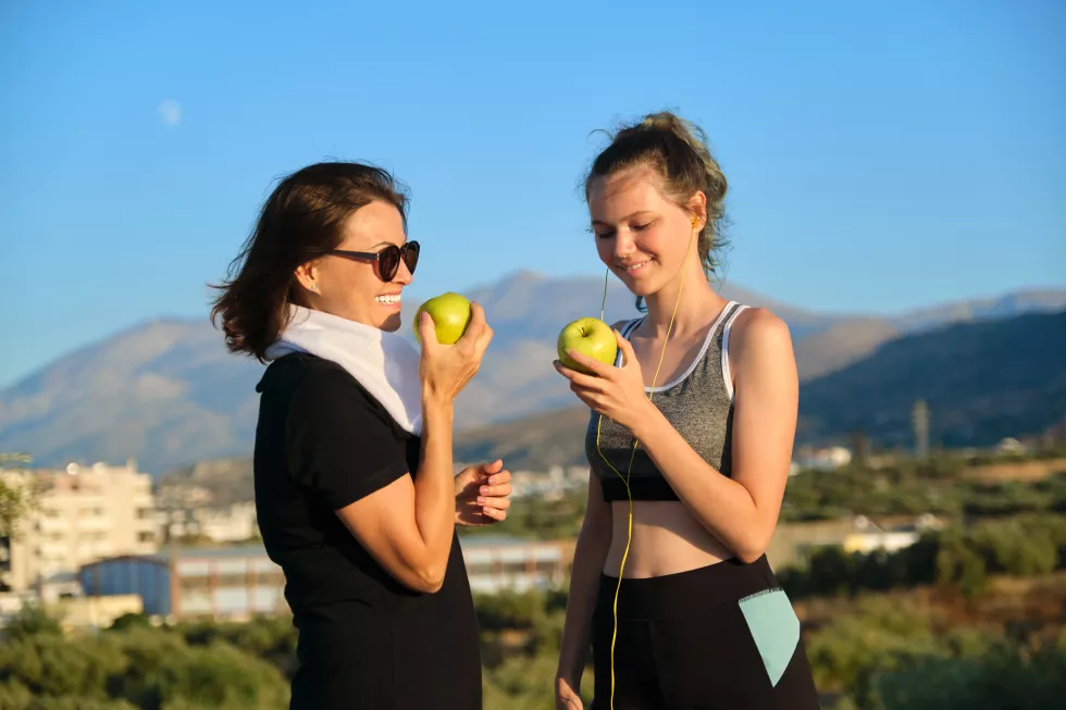 healthy-lifestyle-healthy-food-concept-smiling-fitness-mother-teen-daughter-together-eating-apples-talking-resting-after-athletic-running-outdoor-exercise