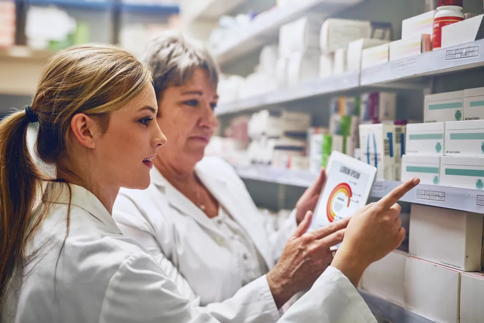 pharmacist-women-together-with-tablet-by-shelf-stock-charts-sales-stats-with-point-inventory-people-mentor-intern-digital-touchscreen-app-inspection-with-graphs-store