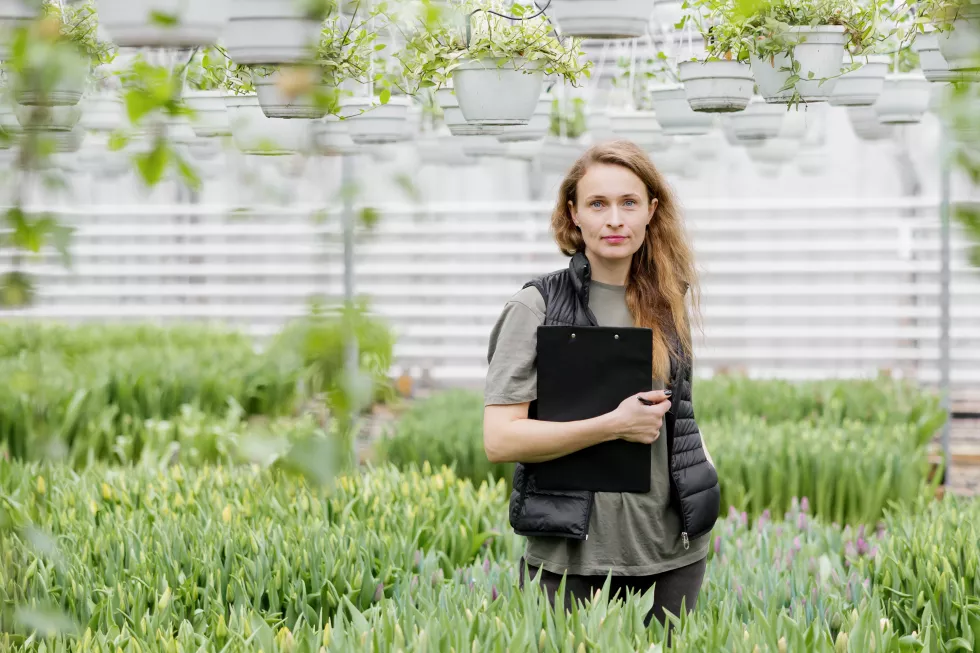young-female-worker-with-copybook-standing-greenhouse-with-tulips