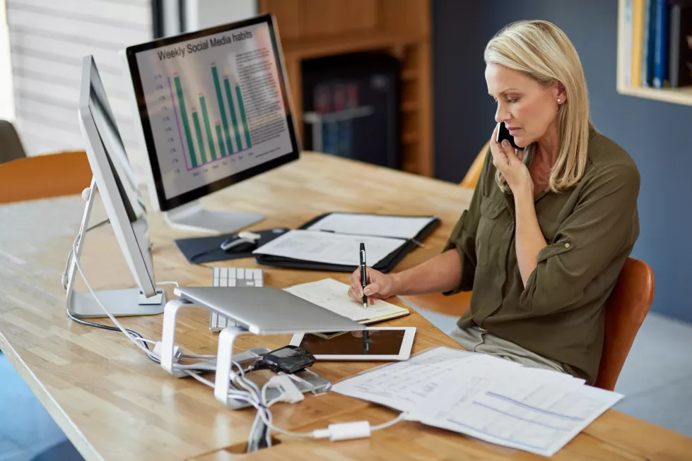 another-busy-day-office-shot-mature-businesswoman-writing-notes-while-talking-cellphone-office