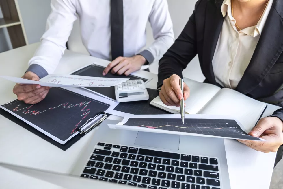 midsection-business-people-discussing-graph-clipboard-with-calculator-laptop-table-office