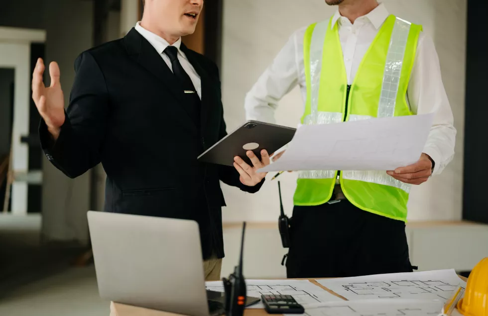 two-colleagues-discussing-data-working-tablet-laptop-with-architectural-project-construction-site-desk-officexa