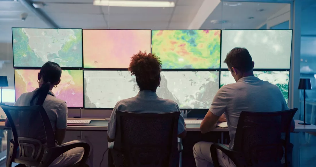 Zespół analizuje mapy pogodowe na monitorach w centrum monitoringu