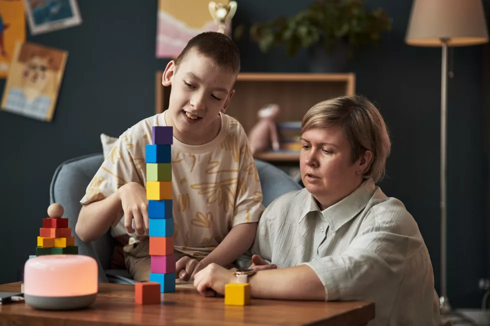portrait-child-with-disability-building-block-tower-with-adult-support