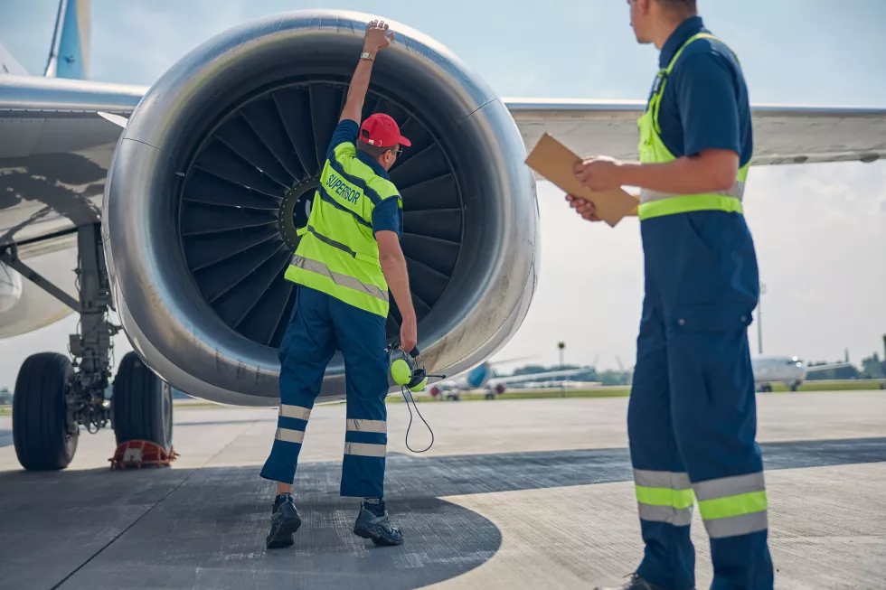 back-view-aircraft-maintenance-engineer-his-colleague-examining-airplane-jet-engine