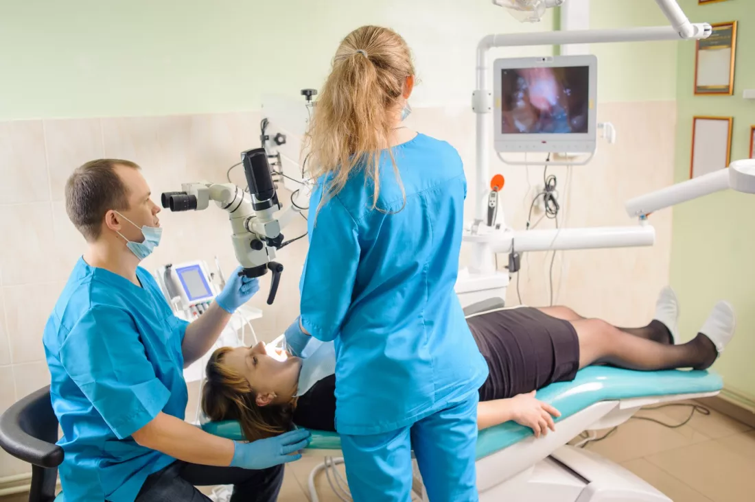 Asystentka stomatologiczna stoi przy fotelu i wspiera lekarza dentyste podczas zabiegu