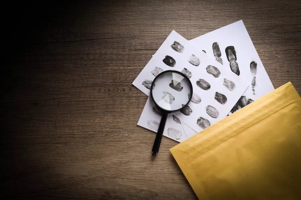 magnifying-glass-with-envelope-with-fingerprints-wooden-background