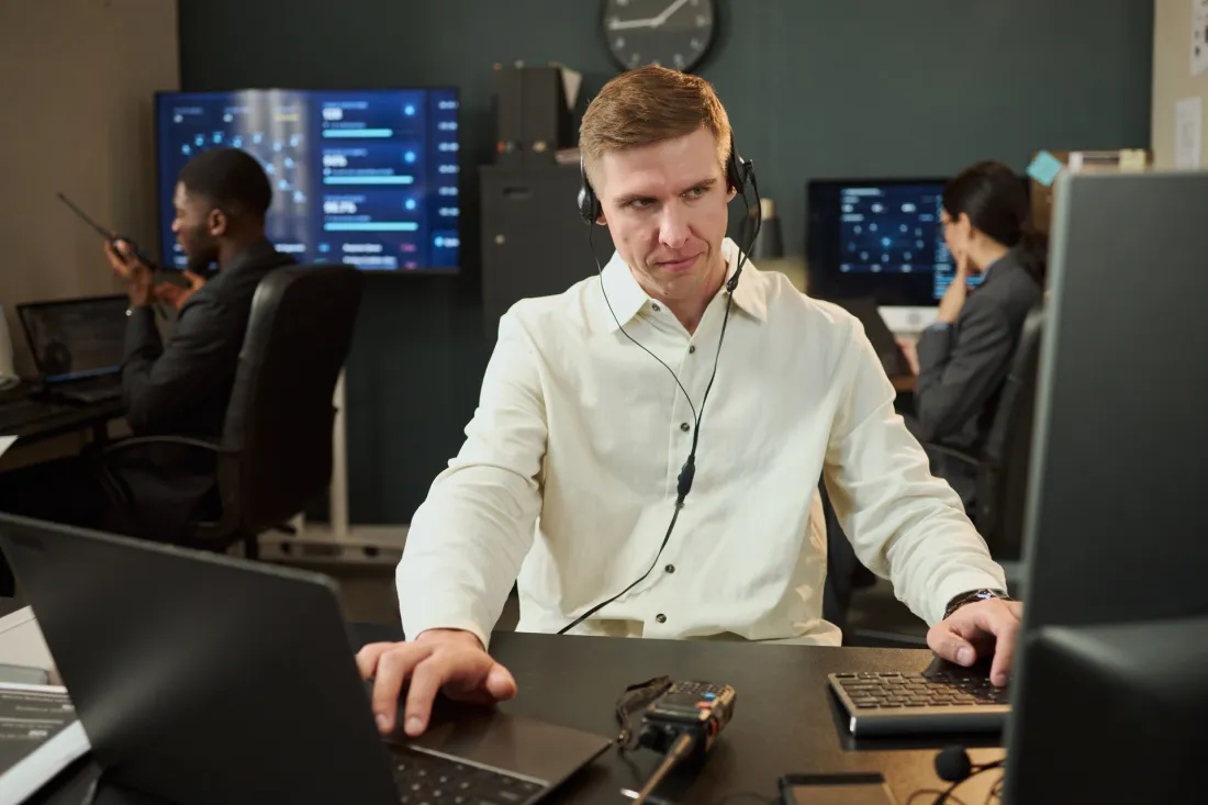 Specjalista ze słuchawkami pracuje przy komputerze w centrum monitoringu z ekranami