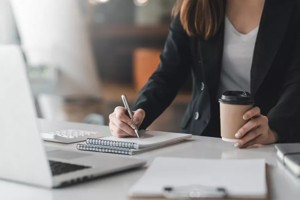 close-up-businesswoman-hand-holding-coffee-mug-while-taking-notes-office