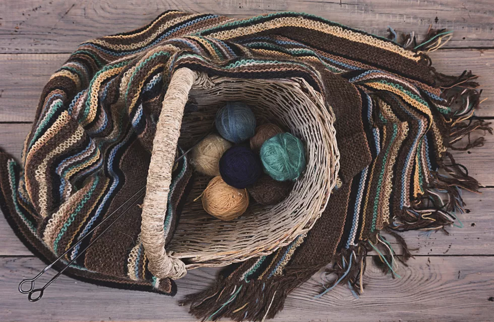 knitted-woolen-scarf-yarn-balls-wicker-basket-wooden-surface
