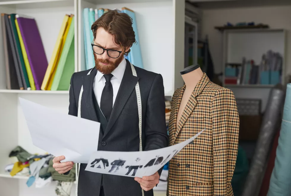 young-bearded-fashion-designer-suit-examining-sketches-new-collection-workshop