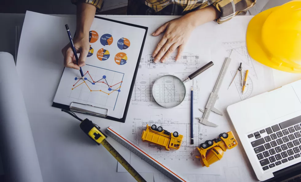 two-colleagues-discussing-data-working-tablet-laptop-with-architectural-project-construction-site-desk-office