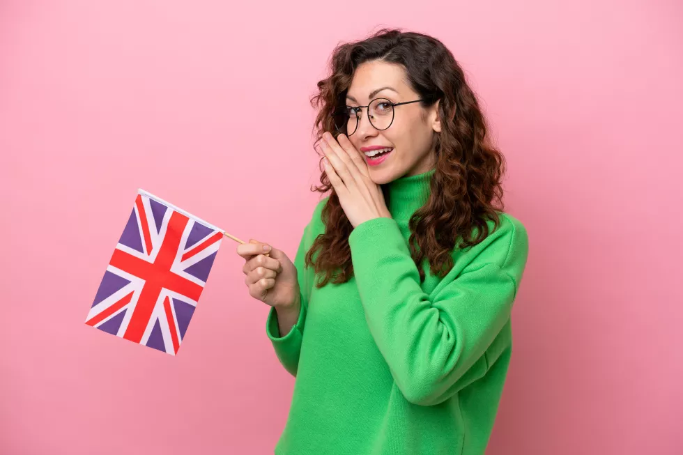 young-caucasian-woman-holding-english-flag-isolated-pink-background-whispering-something