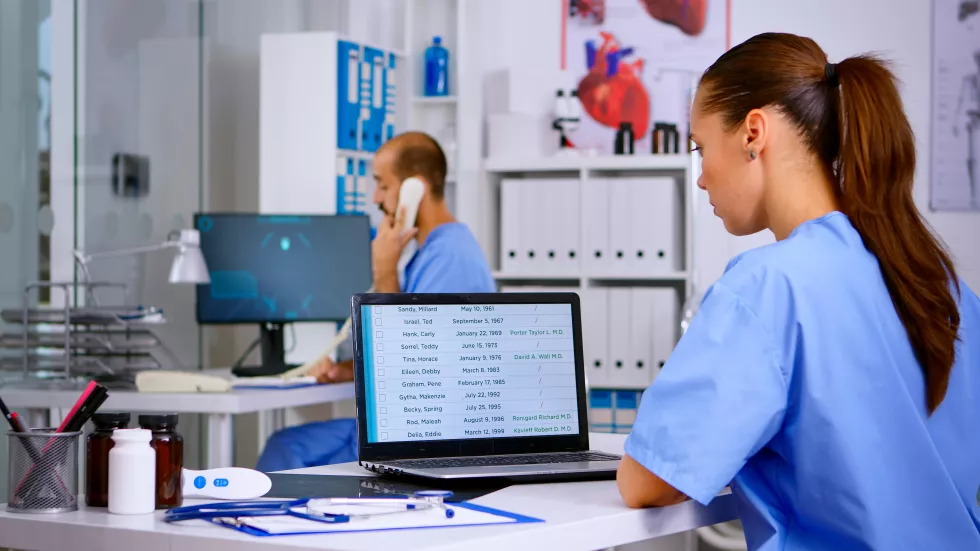 back-view-resident-physician-checking-appointments-laptop-while-coworker-answering-phone-offering-medical-consultation-remote-patient-assistant-working-hospital-clinic