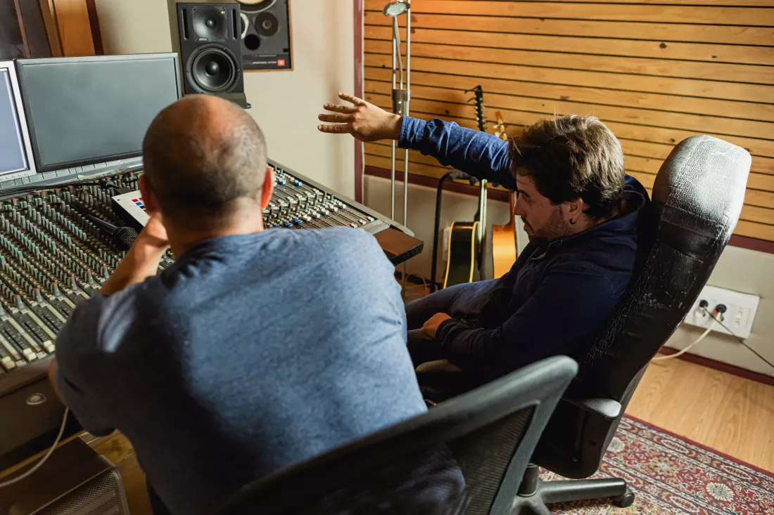 two-men-are-sitting-recording-studio-one-which-is-wearing-blue-jacket