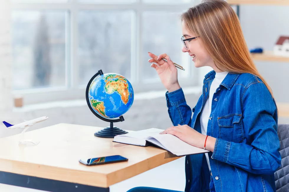 young-caucasian-woman-sits-table-rotates-globe-choose-country-vacation-make-notes-note-book