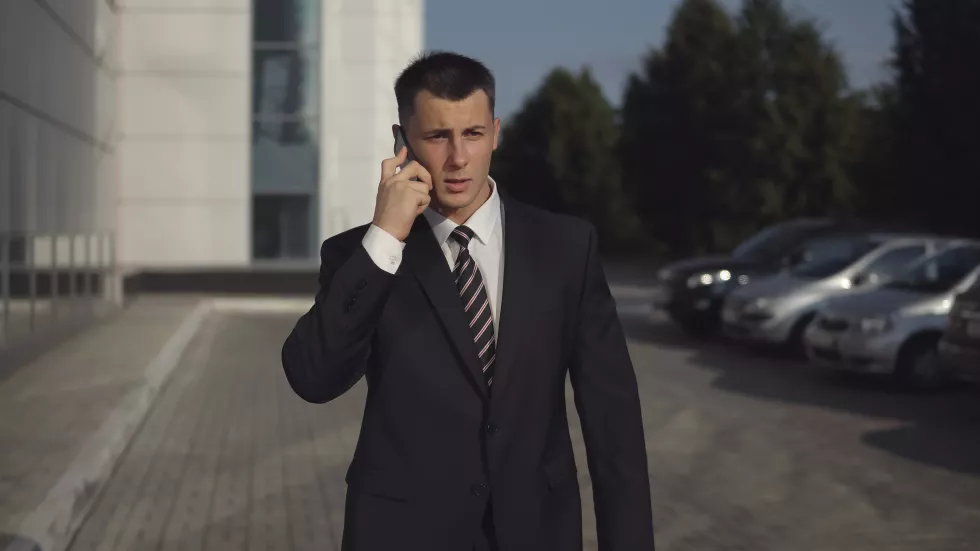 portrait-attractive-slender-businessman-formal-suit-talking-smartphone-against-backdrop-business-center-warm-sunny-day