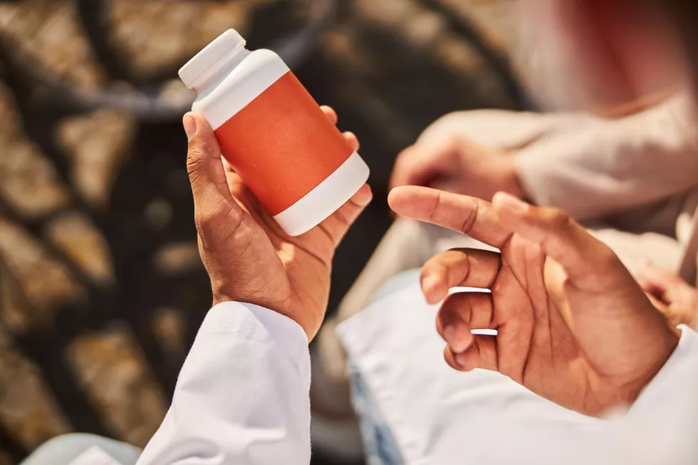 medic-keeping-white-orange-medicine-container-his-hand-while-pointing-it