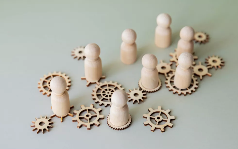 conceptual-image-with-wooden-figures-standing-interconnected-gears