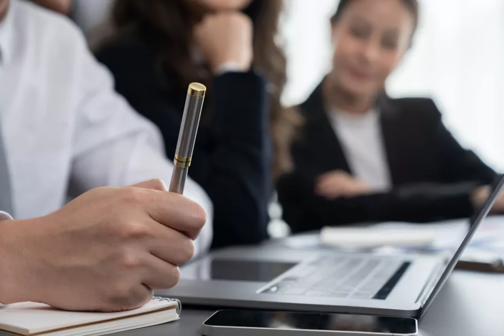 closeup-focus-hand-holding-pen-with-blur-colleague-as-harmony-office-concept
